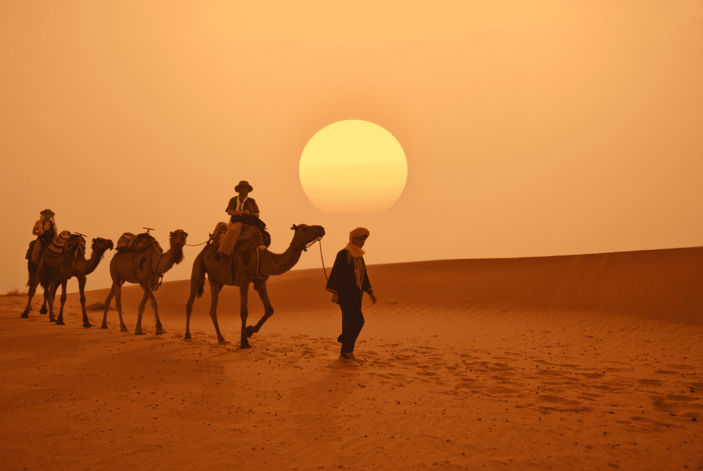 marocká poušť a skupina poutníku s velbloudy