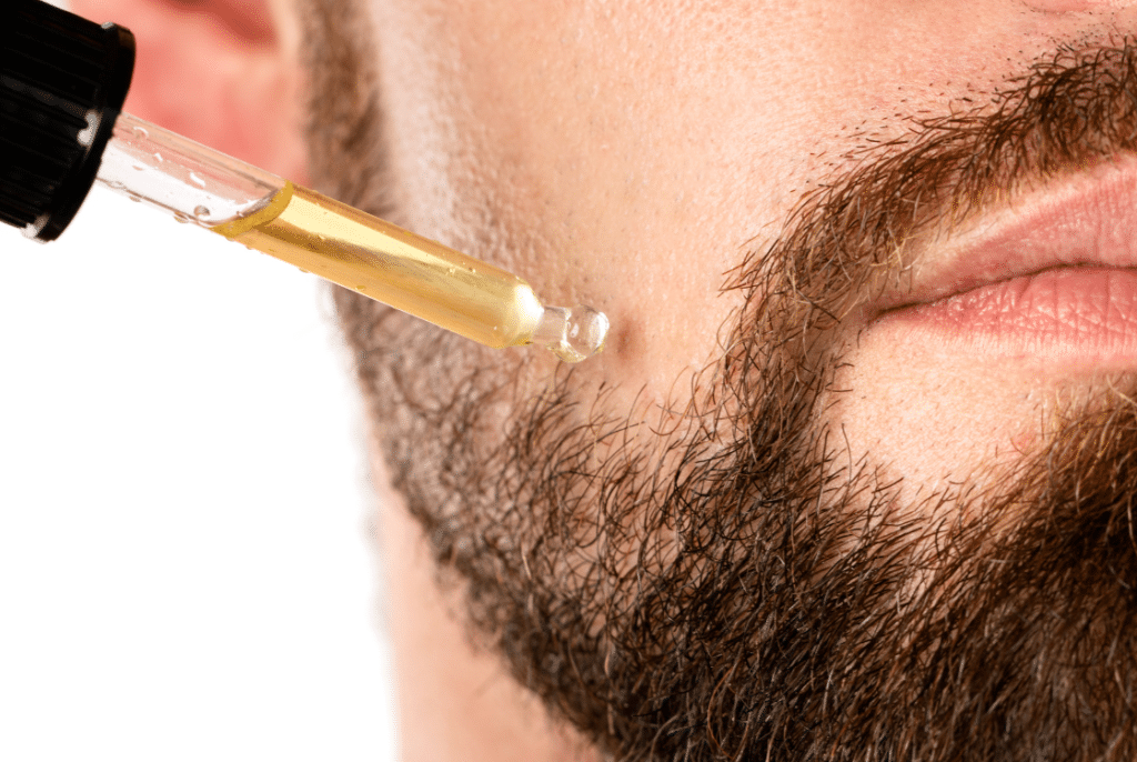 muž s vousy si aplikuje CBD olej na tvář